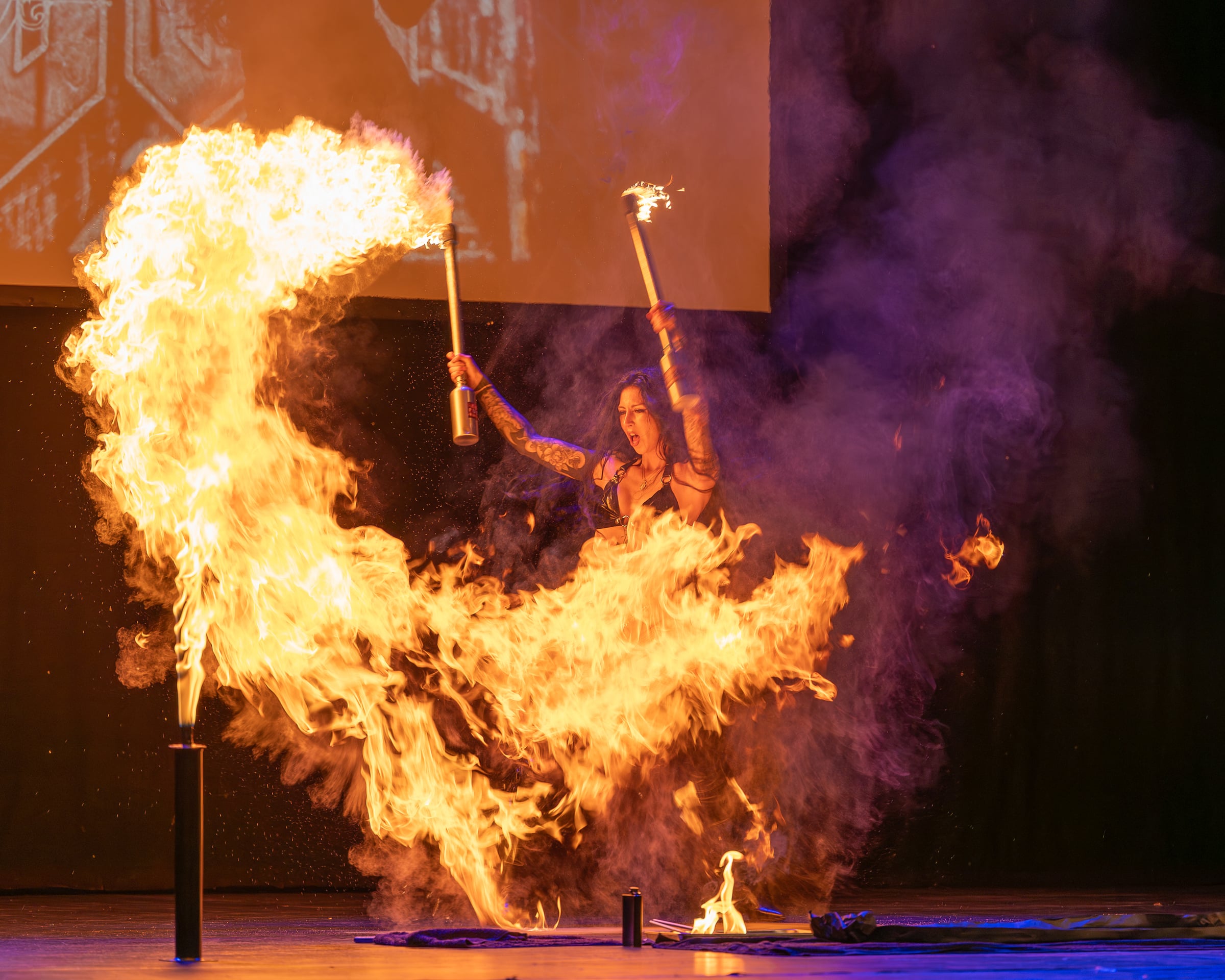 A stage performer surrounded by sweeping flames during a fire performance.
